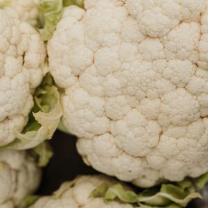 Vertical close-up shot of fresh organic cauliflower with green leaves.
