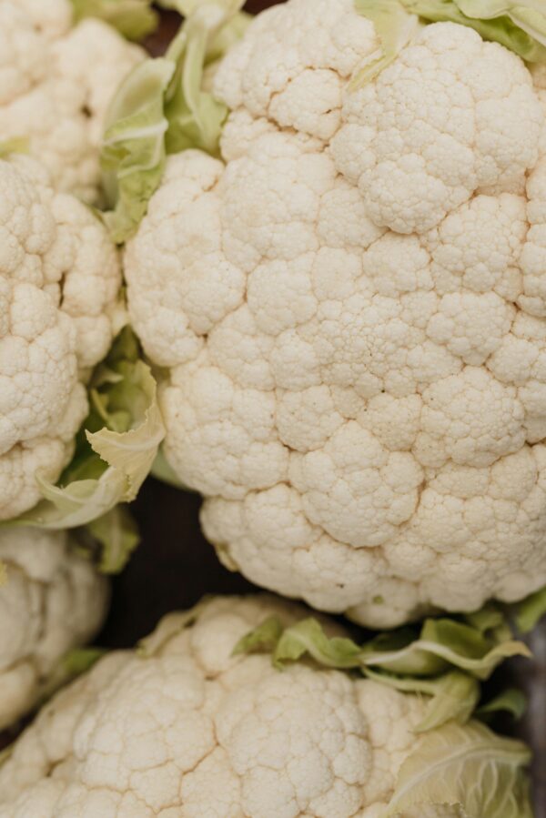 Vertical close-up shot of fresh organic cauliflower with green leaves.
